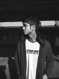 Young man looking away while standing against built structure