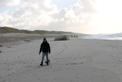 Rear view of mid adult man playing with dog while walking at beach against sky