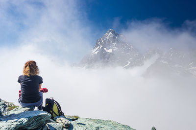 Rear view of woman sitting on rock against sky