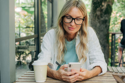 Attractive young woman sitting in a coffee shop has breakfast and uses a mobile phone to communicate