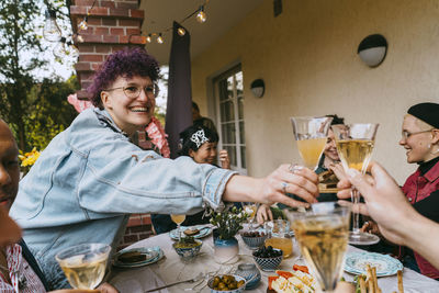 Happy non-binary person toasting drinks with friends during party in back yard