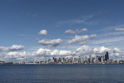 Modern buildings by river against cloudy sky during sunny day