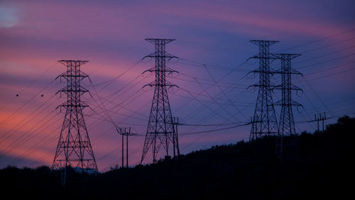 Low angle view of silhouette electricity pylon against sky at sunset