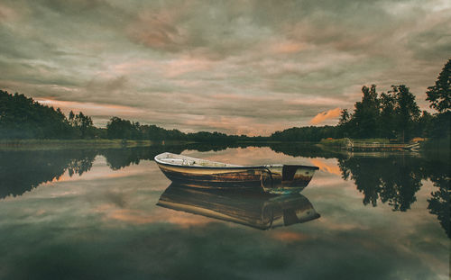 Boat moored on lake against sky during sunset