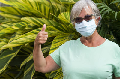 Portrait of senior woman wearing mask standing against plant