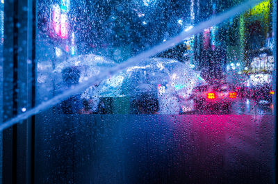 Close-up of wet window in illuminated city at night during rain