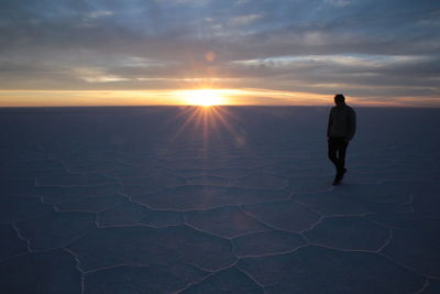 Man walking on salt flat against sky during sunset