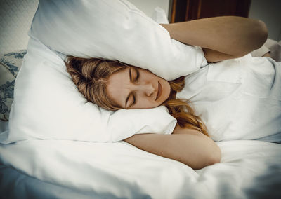 Woman pressing pillow on head while sleeping