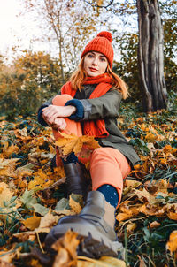 Bright cute young woman in orange warm knitted hat and scarf on background of yellow autumn leaves