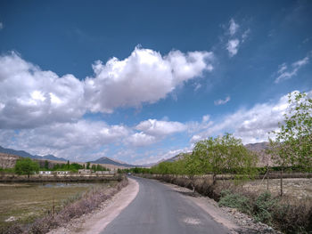 Empty road amidst field against sky