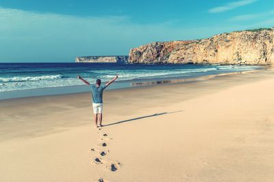 Rear view of person standing on beach against blue sky