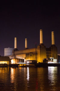 Illuminated battersea power station by thames river against sky