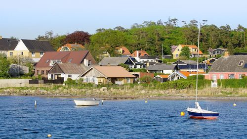 Sailboats moored in river by houses against sky