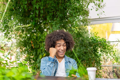 Portrait of young woman using mobile phone while standing against plants