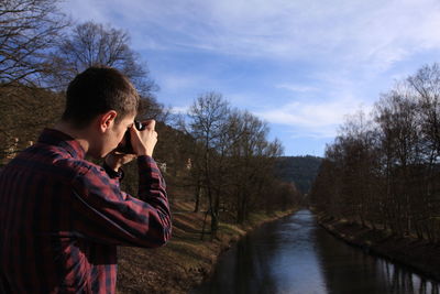 Man photographing trees by lake