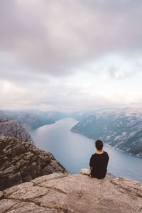 Rear view of man sitting on rock against sky