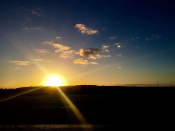 Sun shining through clouds over field