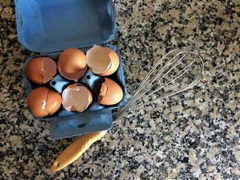 High angle view of broken eggs in carton by wire whisk on marble