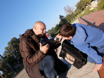Father and son cleaning camera lens with air dust blower at park