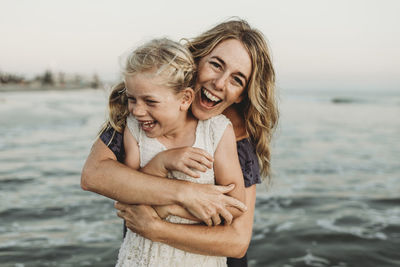 Mother embracing young girl with freckles in ocean laughing