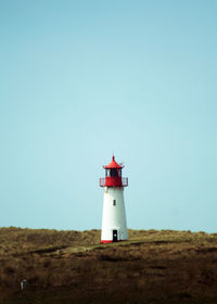 Lighthouse by sea against clear sky