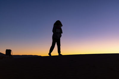 Silhouette woman standing on shore against sky during sunset