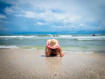 Woman wearing sun hat and lying on her back near the sea on a day with dark storm clouds