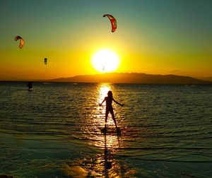 Silhouette person standing in sea against sky during sunset