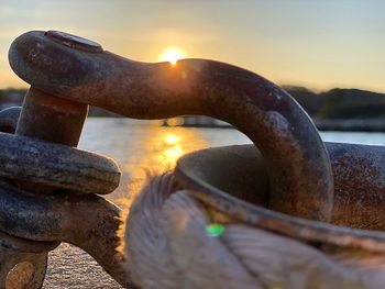 Close-up of rusty metal chain against sky during sunset