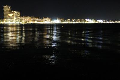 Illuminated buildings by sea against sky at night