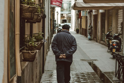 Rear view of man walking on street amidst buildings