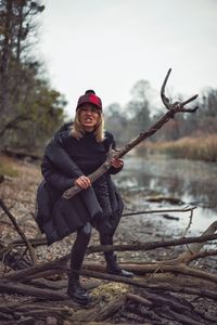 Full length portrait of woman holding stick while standing by river