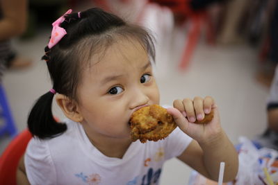 Close-up portrait of cute girl eating chicken meat while sitting indoors