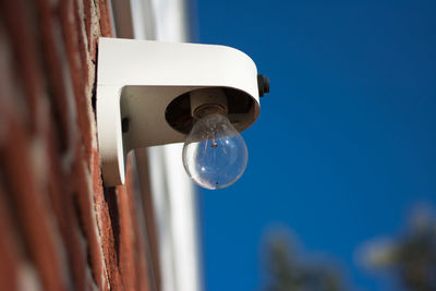 Low angle view of light bulb mounted on brick wall against clear blue sky