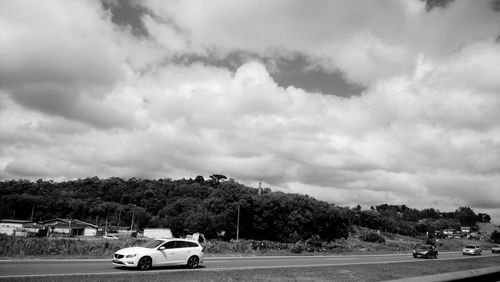 Cars on road against cloudy sky