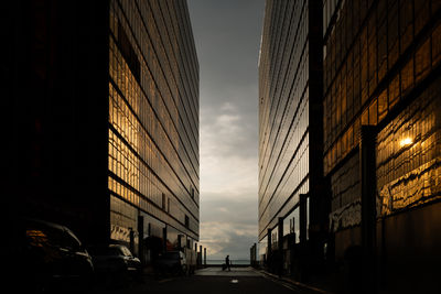 Man walking with a suitcase in between two office buildings during the sunset