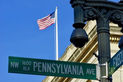 Low angle view of security camera and road sign against american flag