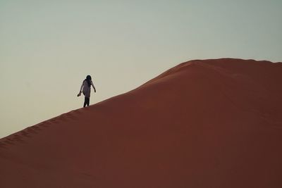 Low angle view of woman walking on sand dune at sahara desert against sky