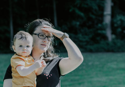 A caucasian baby girl in the arms of a young mother looking into the distance behind other children