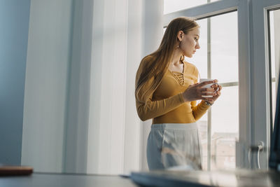 Side view of young woman standing by window