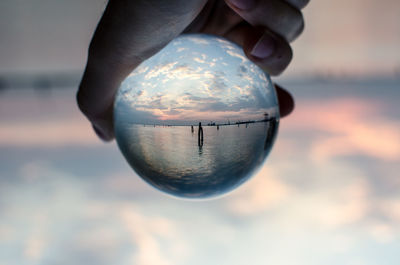 Close-up of hand holding crystal ball against sky