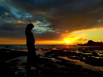 Silhouette man standing on beach against sky during sunset