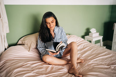 Full length of woman sitting on bed at home