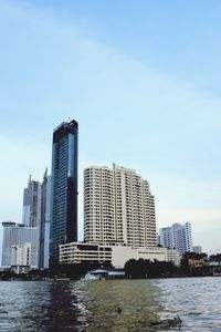 Modern buildings by river against sky in city