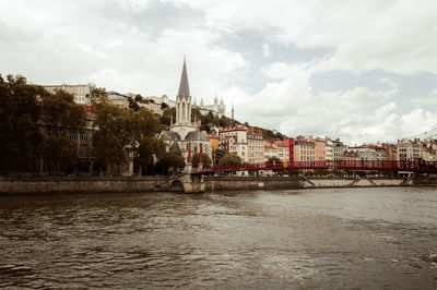 Buildings by river against cloudy sky