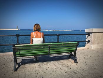 Rear view of man sitting on bench against sea