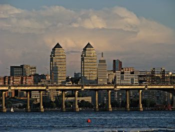 Sea by cityscape against sky during sunset