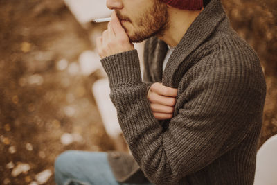 Midsection of young man smoking cigarette while sitting outdoors