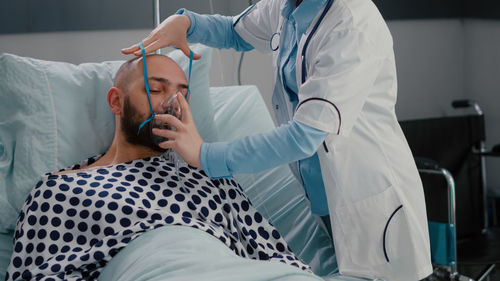 Woman helping patient to wear oxygen mask at hospital