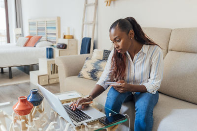 Young woman using mobile phone while sitting on sofa at home